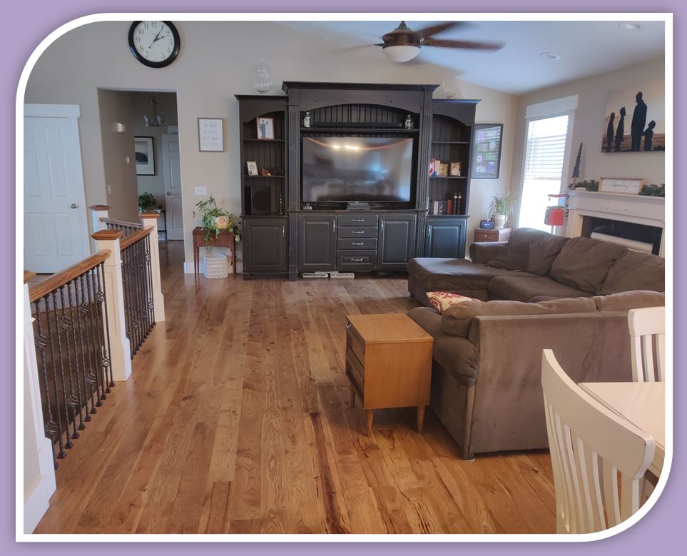 a hickory solid wood floor of traditional design, with Special Walnut colored stain, installed by Hardwood Floorist in a customer's great room. the room contains a large entertainment center with TV and is furnished with a stylish L-shaped sofa.