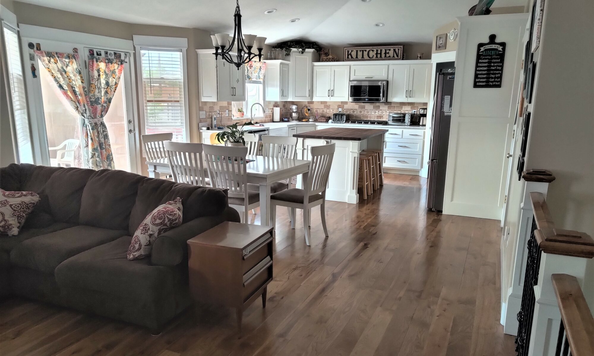 a hickory solid wood floor of traditional design, with special walnut colored stain, installed by Hardwood Floorist in a customer's kitchen. Clean white, cabinetry and counter tops surround the back half of the kitchen, there is an island in the center and a large white table with chairs in the front half.